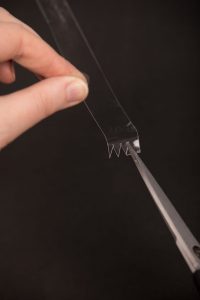 scissors cutting notches into a piece of clear plastic